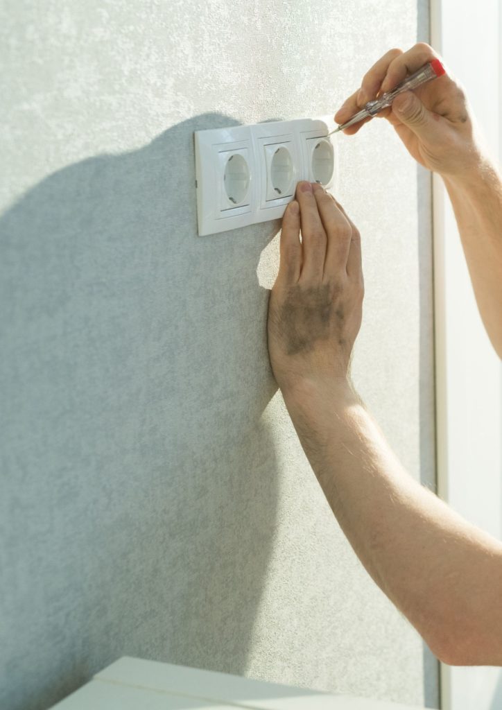 nous voyons deux mains avec un tourne  vise qui bricole 3 prises fixées sur un mur gris.