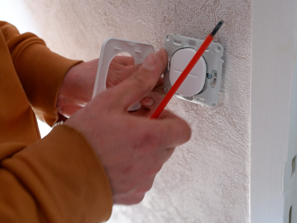gros plan sur les mains de SALOMON Hervé qui fixe un interrupteur a un mur.