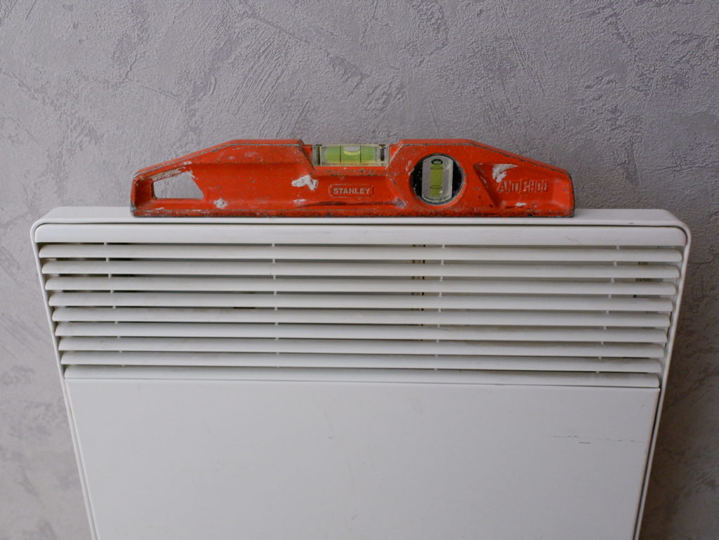 Un radiateur électrique fixé à un mur et un niveau posé dessus pour vérifier qu'il soit bien installer.