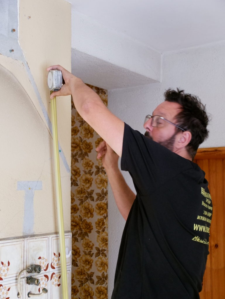 Hervé salomoon qui prend des mesure sur un chantier. il mesure un mur avec un mettre et a un crayon a la main. où va se trouver la prise ? 